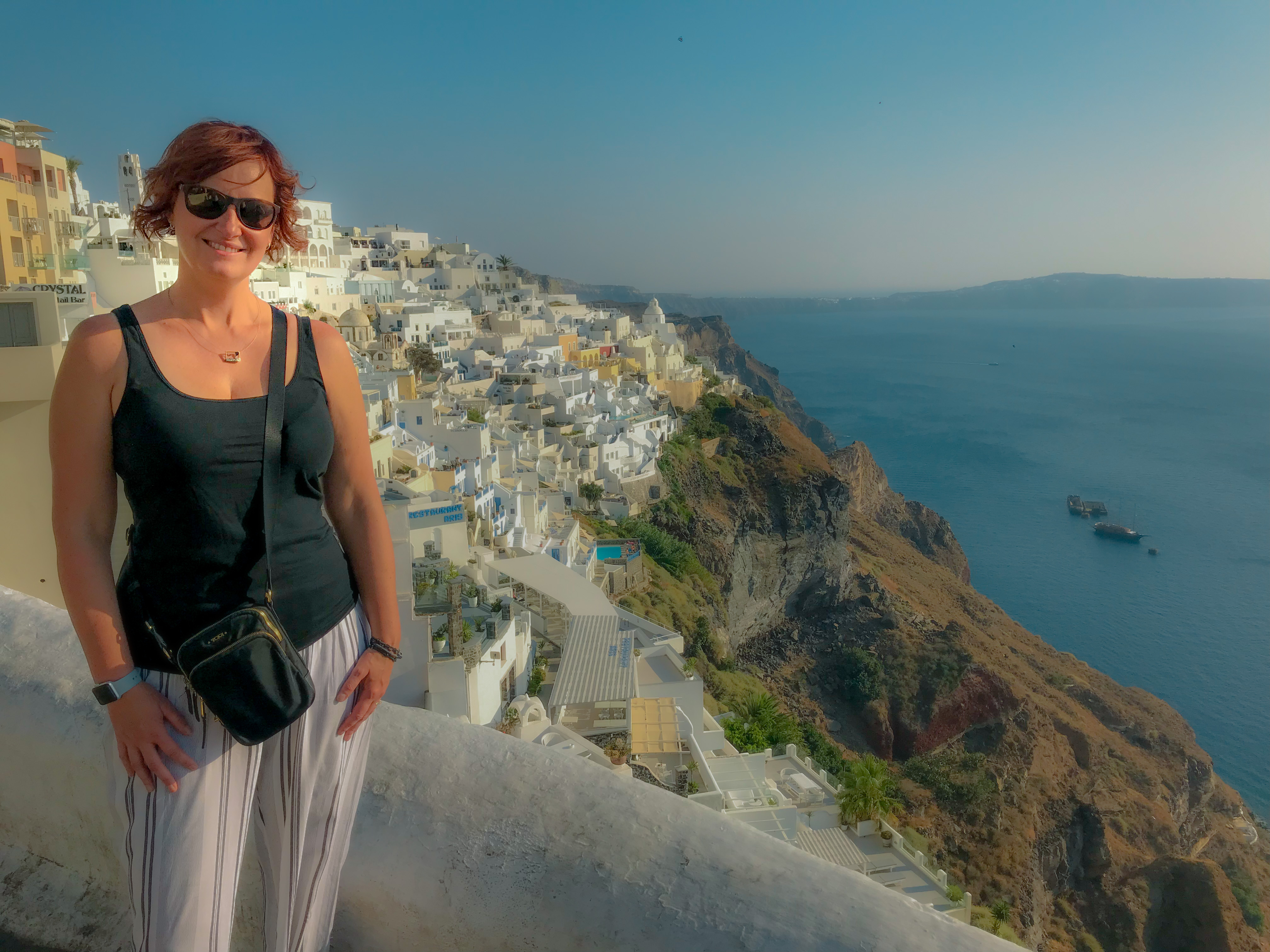 Tamara standing with a view of the whitewashed buildings on the cliffs of Santorini.