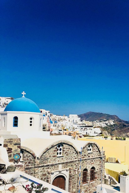 View of Santorini-Champagne with a blue domed church and whitewashed buildings built along the caldera cliffs.