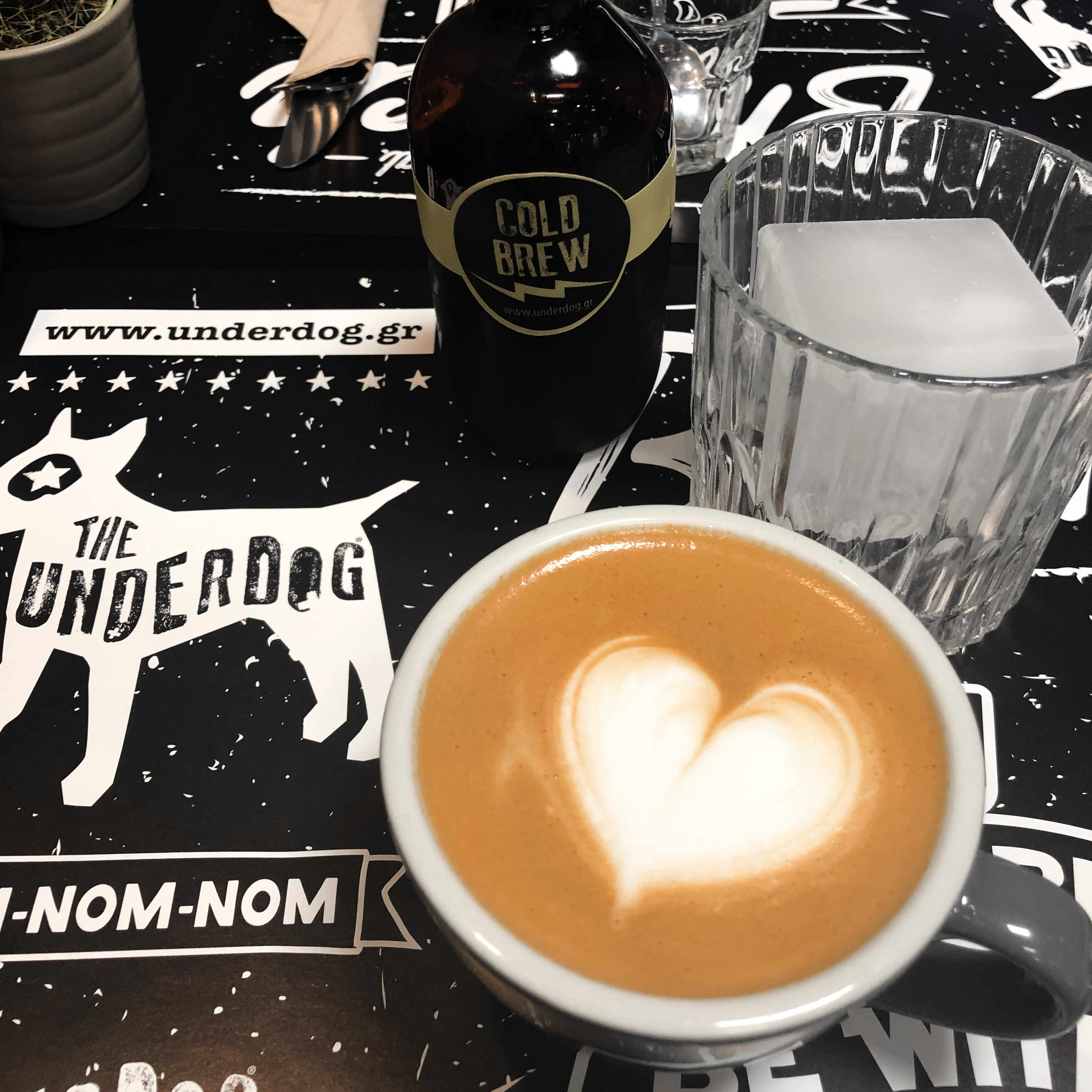 A bottle of the most flavourful cold brew that I have ever tasted along with a glass and a large ice cube to serve it with. Also, a capppuccio with the foam shaped as a heart.  Both drinks were made by The Underdog in Athens, Greece, an award-winning coffee barista.